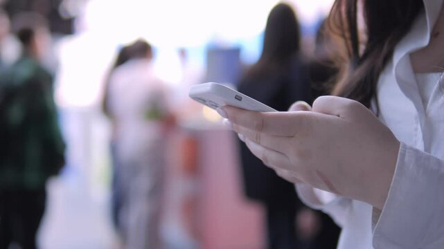 Woman is holding a cell phone in her hand. She is in a crowd of people. Concept of busyness and modern technology