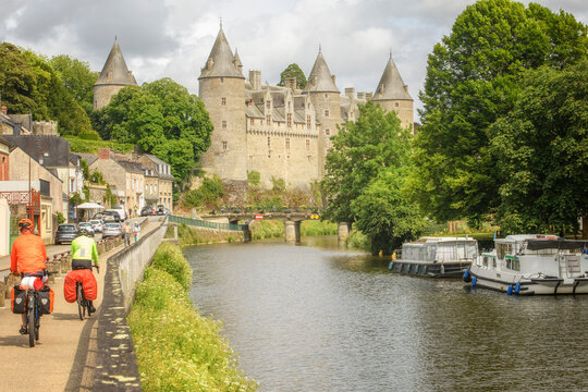 Couple en v&eacute;lo le long d'une riviere avec des peniches et un chateau en arriere plan , velotourisme le long de la riviere Oust sur le canal de Nantes &agrave; Brest, ville de  Josselin en r&eacute;gion Bretagne.