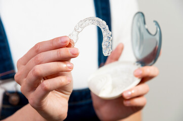 Hands of a Caucasian young woman holding dental aligners and a case for them