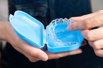 Hands of a Caucasian young woman holding dental aligners and a case for them