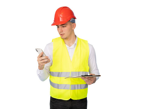 Young construction worker checking smartphone, wearing hard hat, safety vest, holding clipboard against white background