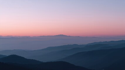 Obraz premium Misty mountain range landscape during a serene pink and purple sunset.