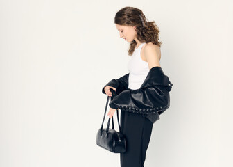 curly-haired elegant woman dressed in office style, in black pants, with a leather jacket and a bag...