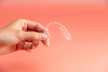 Hand holding plastic braces on pink background. Female hand showing modern methods of teeth straightening