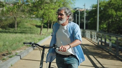 Old Man walking pushing Bicycle in Urban Park. Healthy and active relaxing lifestyle  - Powered by Adobe