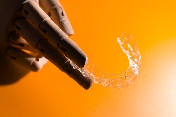 Close-up of wooden elegant hand holding invisible clear aligners, on pastel pink background. Healthy lifestyle and teeth concept