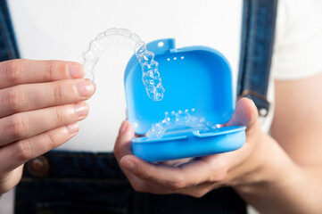 Hands of a Caucasian young woman holding dental aligners and a case for them