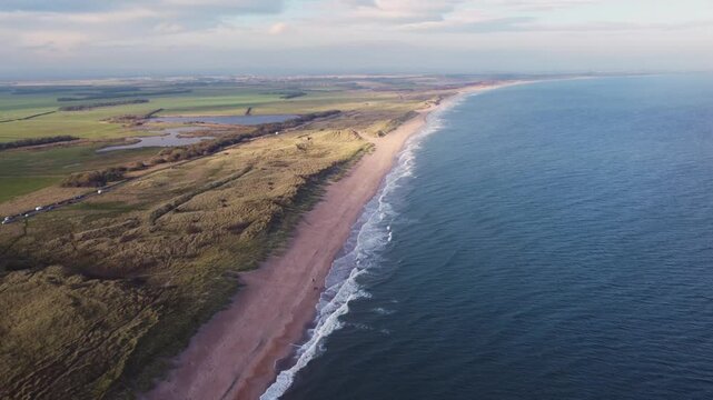 aerial traveling forwards of Cresswell Beach, Druridge Bay, Northumberland with grassy dunes, surf, sandy beach