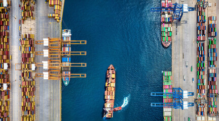 Aerial overhead view of a industrial cargo container terminal port with loading activity by cranes and tug boats moving the ships