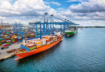 A large container cargo vessel is beeing loaded and unloaded by big cranes in a commercial terminal dock