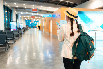 Back view of elegant woman in a hat and jacket, with backpack walks through the airport and using smartphone. Copy space. Concept of boarding at terminal before flight