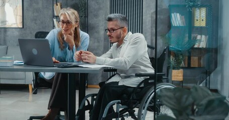 Excited businesswoman and man in a wheelchair trading on stock market celebrate financial profit, looking at laptop and giving high five in modern office. - Powered by Adobe