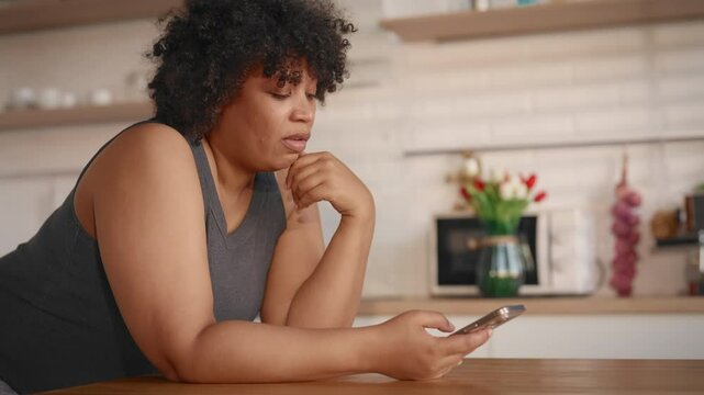 Depressed pregnant woman scrolling social media in mobile app at home, bad mood. Hormonal mood swings, sad emotions and boring, internet addiction and gadget overuse, young black lady with big belly