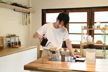A man is pouring coffee into a cup. The coffee is being poured from a black coffee pot. The man is smiling as he pours the coffee.