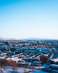 An expansive aerial view of Reykjavik, Iceland, blanketed in pristine snow, with colorful buildings standing out against the white landscape and distant snow-capped mountains