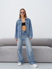 Stylish blonde female model posing indoors in denim outfit with sunglasses