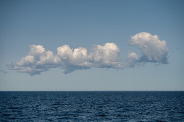 Clouds float above calm ocean water under clear sky at midday in tranquil setting