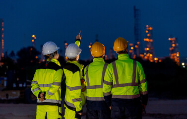 Fototapeta premium Back of group of petrochemical or gas factory stand in front of factory with show working light at night.