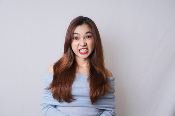 Beautiful blonde Asian woman with make-up wearing light blue off-shoulder top doing silly facial...