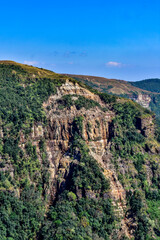 Jagged cliffs and lush green mountains in Meghalaya, India, under a blue sky.