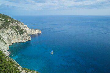 Fototapeta premium A barefoot traveler strolls along a sun-heated stone path surrounded by olive trees in Zakynthos. The vintage postcard of Navagio ghost ship evokes a nostalgic Mediterranean summer