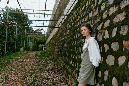 Young woman in casual style stands against a stone wall, showcasing natural beauty and relaxed emotions in a serene outdoor setting