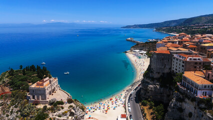 Obraz premium Aerial view of Tropea, Calabria, with turquoise Tyrrhenian Sea, sandy beach, colorful umbrellas, and Sanctuary of Santa Maria dell'Isola