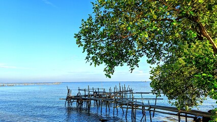 Scenic view of calm blue sea with bamboo bridge under shady tree at Alar Beach, Tangerang, Indonesia