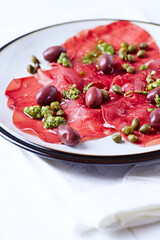 Slices of beef carpaccio with olives and capers. Close up.