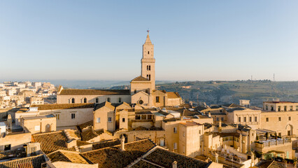 Aerial view of Matera, Italy, bathed in golden morning light. The iconic stone dwellings and cathedral tower rise above the canyon, showcasing this UNESCO-listed historic wonder