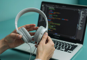 White headphones are held near a laptop displaying lines of code on a turquoise surface