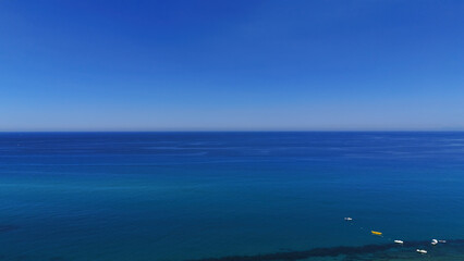 Tranquil aerial view of the Tyrrhenian Sea near Tropea, Calabria, with boats dotting the clear blue water under a vast, vibrant sky