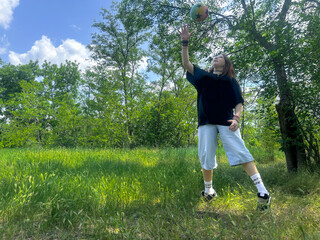 Young woman playing with ball outdoors on a sunny day. Active girl enjoying outdoor activity in nature, summer lifestyle concept.