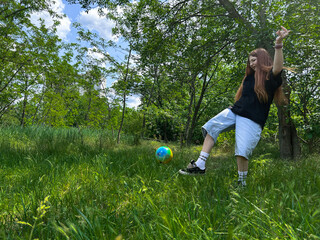 Young woman playing with ball outdoors on a sunny day. Active girl enjoying outdoor activity in nature, summer lifestyle concept.