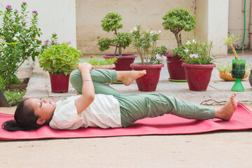 Indian girl doing Pawanmuktasana yoga, relaxing in one Knee to Chest pose. she shows flexibility and focus while engaging in traditional yoga