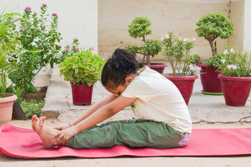 Indian Girl Child Practicing Paschimottanasana, also known as the Seated Forward Bend Pose Yoga  outdoors in the fresh air. promotes spine flexibility, digestion, and inner peace. 