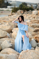 Beautiful young girl with long dark hair in a blue long dress on the beach at sea in summer