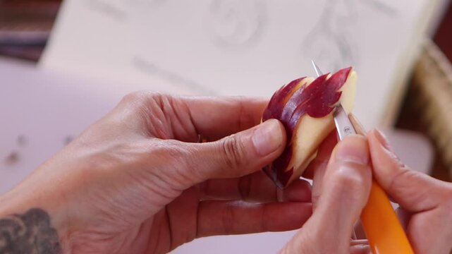 A chef is carving an apple into Thai patterns with a stencil knife.
