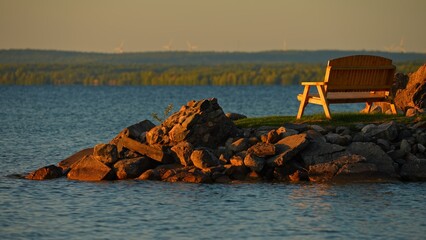 Romantic view of empty bench at small boat bay of Lake Manitou, golden hour sunset dusk. Nestled in the quiet charm of tranquil water. Golden light casts its enchanting glow, the romantic ambiance.