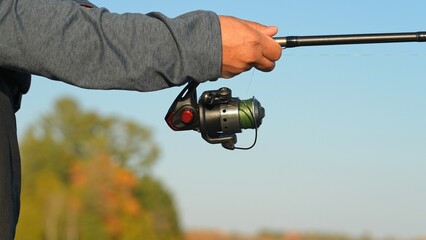 Close up of unrecognizable woman spinning fishing reel at the lake in North America. Women angler holding fishing rod with braid. Fisherwoman spins the reel on a spinning rod.