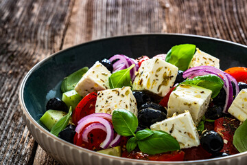 Greek style salad - tomatoes, cucumber with feta cheese, basil leaves and black olives on wooden table	

