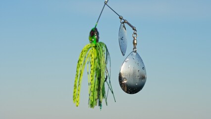 Bass and Pike fishing lure selective shallow close up focus. Spinner bait jig with spoon rotation against blue sky. Fishing equipment with artificial small fish bait.