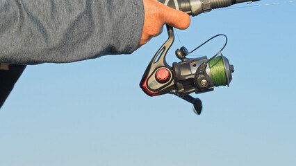 Woman fishing and cast fishing tackles gear, reel and rod with green braid. Fish game leisure activity during vacation at the lake. Relax and hobby. Angler with rod and spinning wheel catching pike.