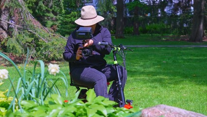 Videographer or photographer with physical disability, taking a photo of nature and enjoying spring. Cinematic shot of multiethnic independent semi professional content creator on the mobility scooter