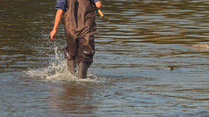 Unrecognizable Fisherman or Angler walks in the wader and wading boots at the slippery rocky rapid river or creek for the salmon and trout spot to fish. Fishing game and sport for fisherman.