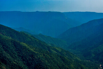 Layers of verdant Meghalaya mountains fade into a hazy blue horizon under a clear sky.