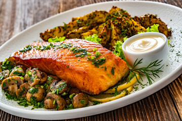 Seared salmon steak with champignons, mayonnaise and baked potatoes on wooden table	