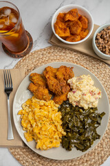 Home cooked meal plate of southern cooked food including collard greens, potato salad, fried chicken, macaroni and cheese, black eyed pies, candied yams and sweet tea