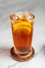 A single glass of cold sweet, iced tea photographed on a white marble background