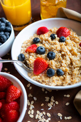 Bowl of oatmeal with blueberries and strawberries on rustic dark wood chopping board